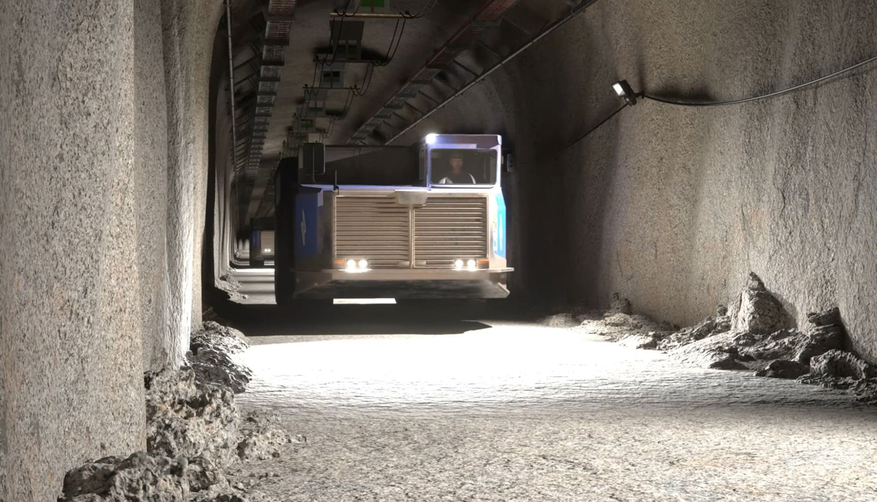 Heavy mining truck driving through an underground tunnel with dim lighting and rough rock walls.